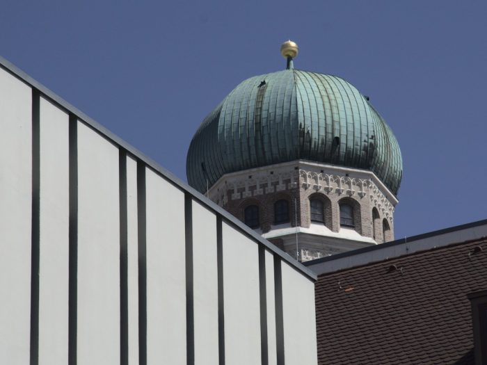 Turmspitze der Frauenkirche in München zwischen Häusern